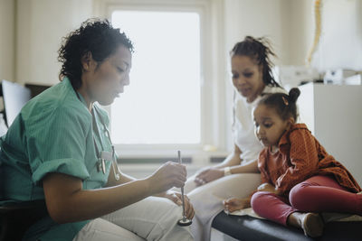 Female pediatric holding reflex hammer discussing with patient in hospital