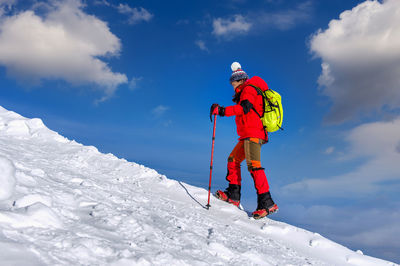 Side view of female hiker walking on snow covered field against sky