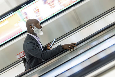 Senior businessman with smart phone moving up on escalator at subway station