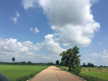 Empty road amidst field against sky