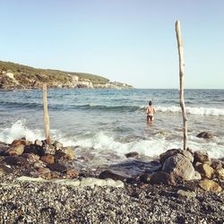 Man standing on rock at beach against clear sky