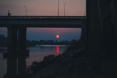 Silhouette bridge over river against sky during sunset