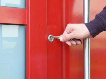 Cropped hand of person holding key over hole on closed red door