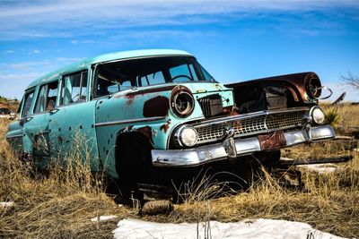 Abandoned vehicle in tall grass, rusting as snow melts on a warm winter day