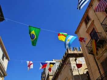 Low angle view of flags hanging amidst buildings against clear blue sky