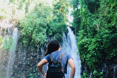 Rear view of woman looking at waterfall in forest