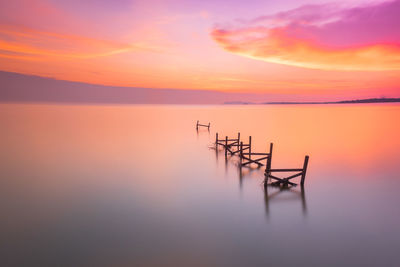 Wooden posts in sea against sky during sunset