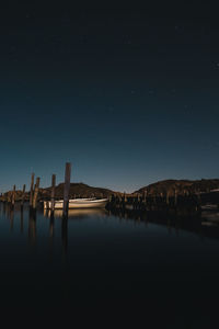 Wooden posts in lake against sky at night