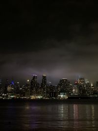 Illuminated buildings by river against sky at night