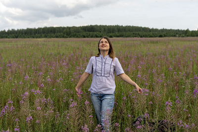 Happy beautiful smiling blond young woman in purple shirt on meadow of fireweed flowers looking up 