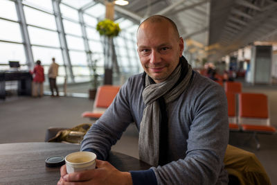 Portrait of smiling man holding disposable coffee cup while sitting at chubu centrair international airport