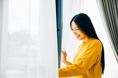 Young woman looking through window at home
