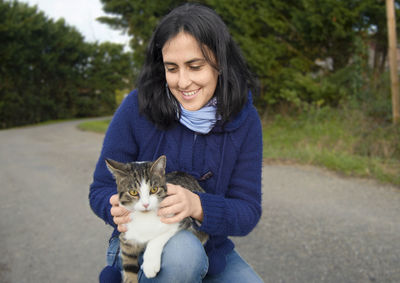 Young woman stroking cat while crouching on country road