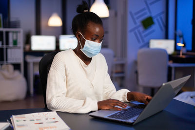 Businesswoman wearing mask working on laptop at home