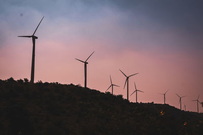 Silhouette wind turbines on field against sky during sunset