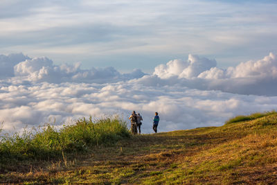 Friends standing on mountain against cloudy sky