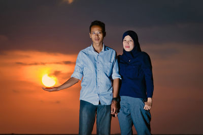 Young couple standing against orange sky during sunset