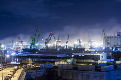 Cranes at harbor against sky at night