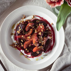 Home-made salad on a white plate, made with beets and blood oranges, topped with nuts and herbs.