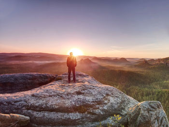 Moment of loneliness. sportsman with hands in pockets stand on the rock peak and watching sunset.