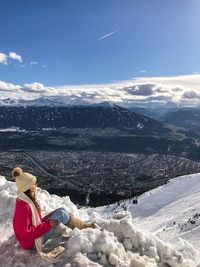 Side view of woman sitting on snow at mountain peak against sky