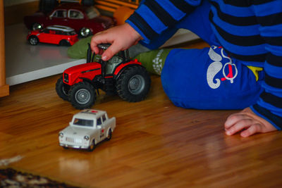 Low section of boy playing with toy car on hardwood floor