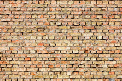 Texture of an old brick wall with potholes, cracks and various damages.