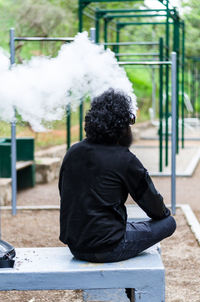 Rear view of man smoking while sitting outdoors