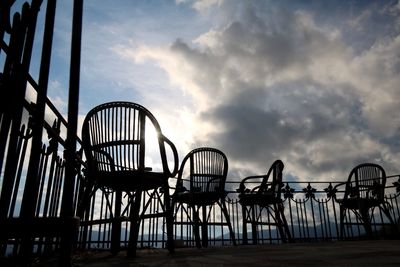 Silhouette empty wooden chairs at balcony against cloudy sky