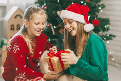 Two happy and beautiful teenage girls in new year's outfits open gifts at home 
