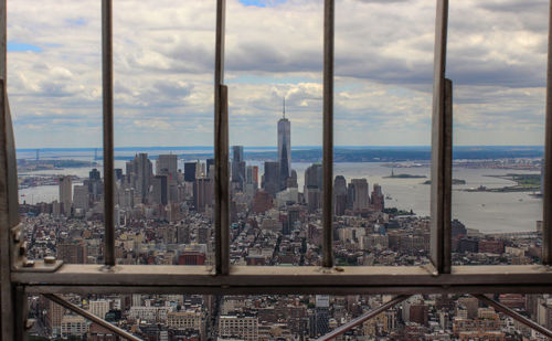 Cityscape with one world trade center by river seen through fence