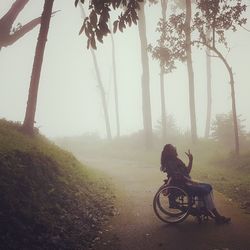 Woman gesturing peace sign while sitting on wheelchair during foggy weather