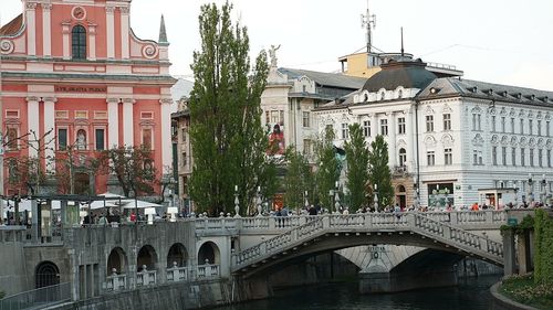 Bridge over river by buildings in city against sky