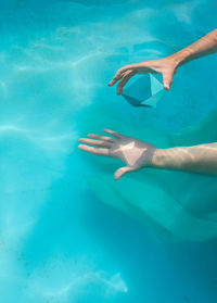 Cropped hand of woman holding pyramid crystal in swimming pool