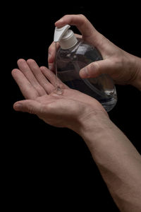 Close-up of hand holding bottle against black background