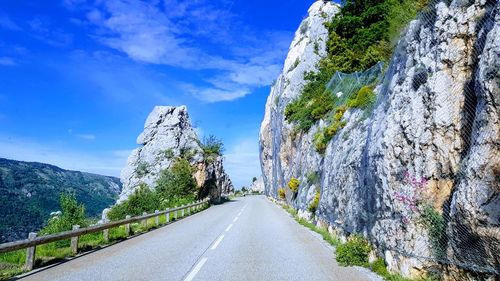 Empty road amidst plants against blue sky