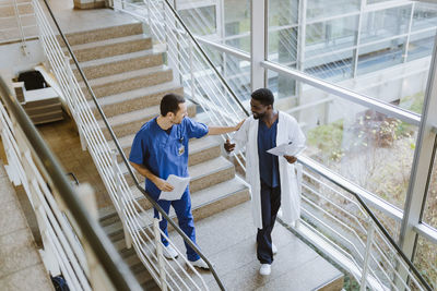 High angle view of smiling male doctor and nurse discussing while moving down on staircase in hospital