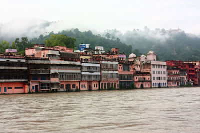 Pink buildings on riverbank against misty mountain backdrop