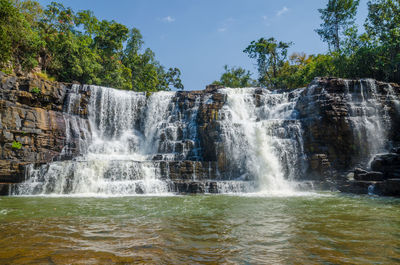 Low angle view of waterfall in forest against sky