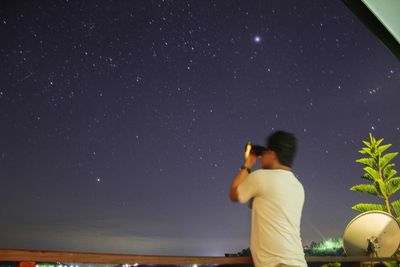 Rear view of man photographing against sky at night