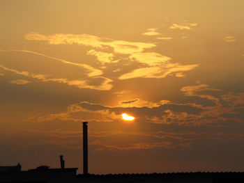 Silhouette of factory against orange sky