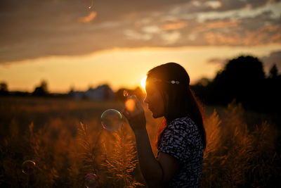 Silhouette woman holding flower on field against sky during sunset