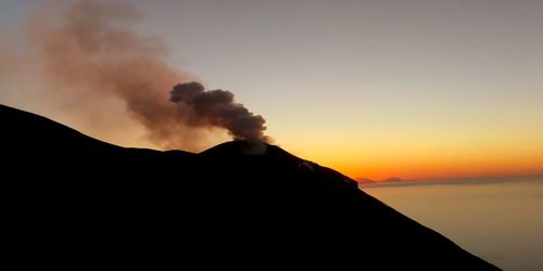 Smoke emitting from volcanic mountain against sky during sunset