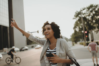 Woman hailing while standing on city street against sky