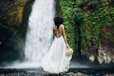 Rear view of woman standing by waterfall