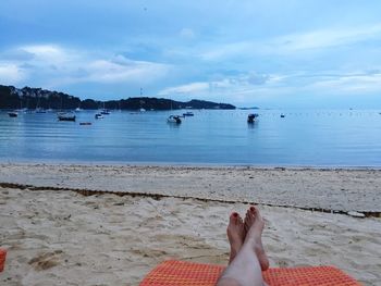 Low section of woman relaxing on beach against sky