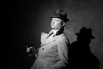 Tilt shot of gangster holding gun against wall at night