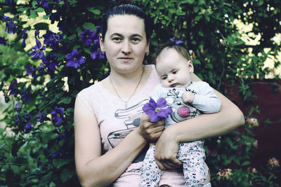 Portrait of mother carrying cute daughter while standing against plants at park