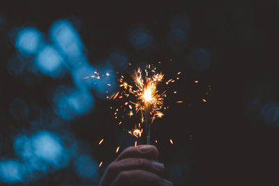 Cropped hand holding illuminated sparkler at night