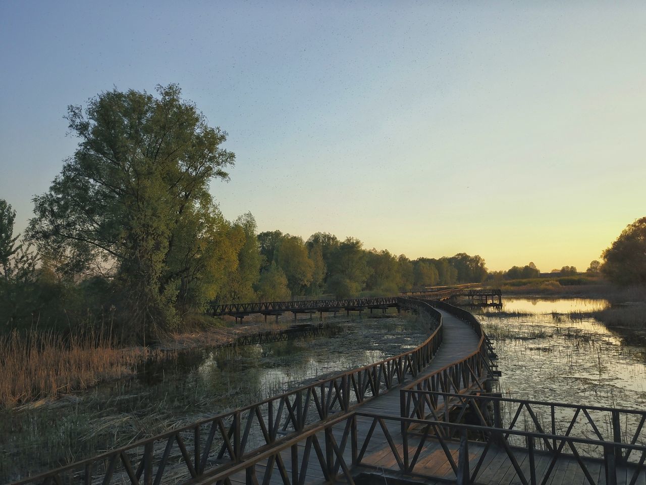 BRIDGE OVER RIVER AGAINST CLEAR SKY DURING SUNSET